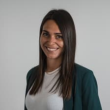 Donna con lunghi capelli castani, blazer verde scuro su top bianco, sorride in un ritratto in studio.