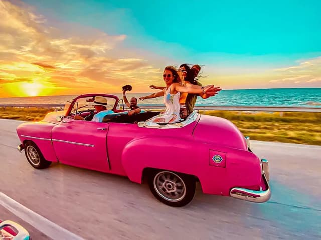Viajeros de WeRoad en un coche clásico rosa al atardecer en Cuba