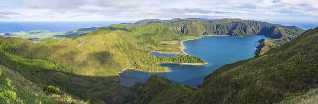 Panoramablick auf einen tiefblauen See in einer vulkanischen Caldera, umgeben von üppig grünen Bergen und dem fernen Ozean.