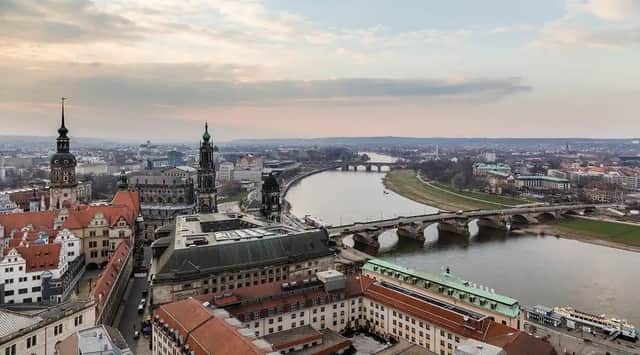 An aerial view of a historic European city with a wide river, several stone bridges, and ornate architecture under a cloudy sky.
