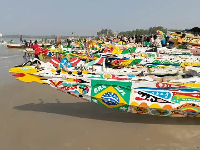 Una flota de barcos de pesca de madera intrincadamente pintados descansando en una playa de arena con gente reunida al fondo.