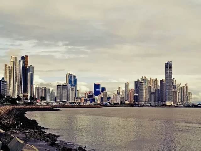 Skyline moderno di città con numerosi grattacieli, visto da una costa rocciosa oltre l'acqua sotto un cielo nuvoloso.