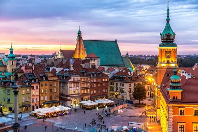 An elevated view of a historic European city square at dusk, with people walking below and dining at outdoor cafes.