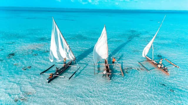 Vue aérienne d'un voyage de groupe WeRoad naviguant sur trois pirogues traditionnelles à balancier sur des eaux peu profondes et turquoises.