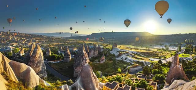 Dutzende Heißluftballons schweben bei Sonnenaufgang über einem Tal mit einzigartigen Felsformationen und einem Dorf.