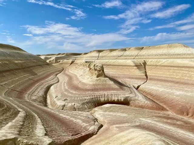 Colorate formazioni rocciose stratificate di sedimenti rossi e bianchi formano dolci colline in un canyon sotto un cielo blu.