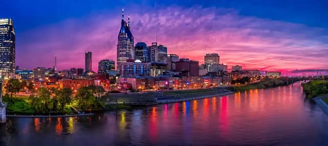 Uno skyline cittadino illuminato si riflette in un ampio fiume al tramonto sotto un cielo vivace rosa e viola.