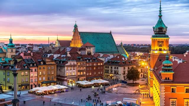 Una vista elevada de una plaza histórica de ciudad europea con edificios coloridos y una catedral, iluminada al atardecer.