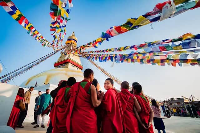 Eine Gruppe rotgekleideter Mönche versammelte sich vor einer großen weißen Stupa, darüber wehten bunte Gebetsfahnen unter blauem Himmel.