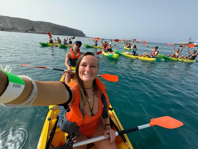 Eine Frau macht in ihrem Kajak ein Selfie während einer WeRoad Gruppenreise auf See, mit anderen Kajakfahrern im Hintergrund.