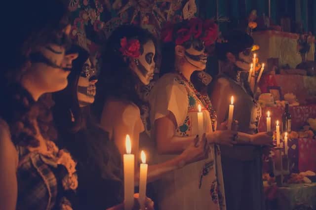 Un viaggio di gruppo WeRoad di donne con make-up da teschio che tengono candele accese davanti a un altare del Giorno dei Morti.