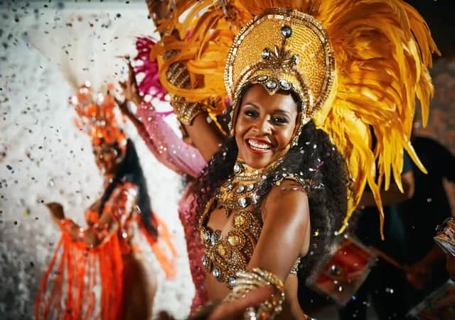 Une femme souriante, vêtue d'un costume de carnaval doré et emplumé, danse tandis que des confettis tombent autour d'elle.