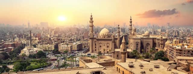 Vista panorámica de una gran mezquita con cúpulas y minaretes, dominando un denso paisaje urbano bajo un atardecer dorado y brumoso.