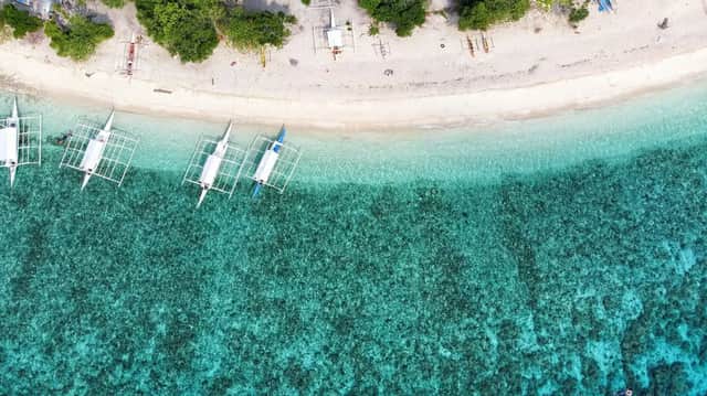 Vista aérea de varias canoas con balancín amarradas en una playa de arena blanca junto a agua turquesa.
