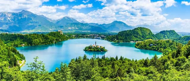Panoramablick auf eine Kirche auf einer kleinen Insel inmitten eines ruhigen, blauen Sees, umgeben von Wäldern und Bergen.