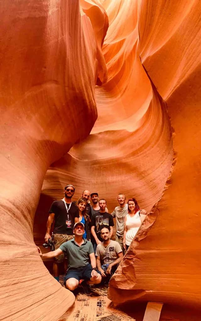 Un viaje en grupo de WeRoad posando para una foto dentro de un estrecho cañón de ranura naranja con paredes de roca lisas y onduladas.
