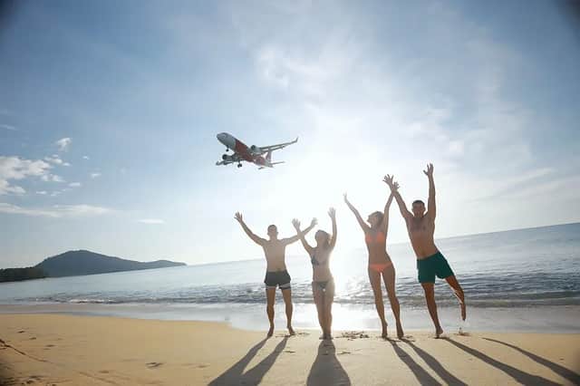 Un viaggio di gruppo WeRoad di quattro persone che salutano con le braccia alzate un aereo che vola basso su una spiaggia assolata.