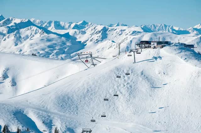 Un télésiège s'élève sur une montagne enneigée vers une station de sommet, avec une vue panoramique sur une chaîne de montagnes enneigée.