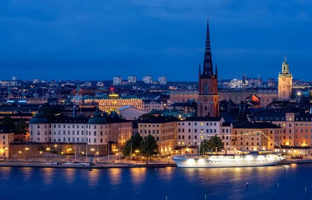 Un panorama urbano illuminato con un'imponente guglia di cattedrale, visto dall'altra parte dell'acqua al tramonto, con una nave attraccata lungo il lungomare.