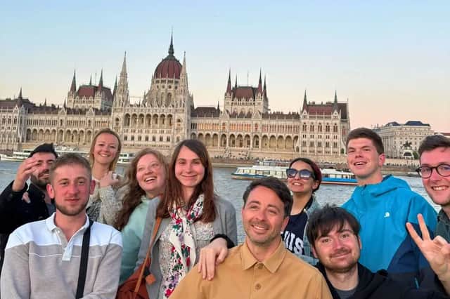 Un voyage de groupe WeRoad souriant ensemble pour une photo devant un grand bâtiment gouvernemental orné sur une rivière au crépuscule.