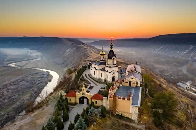 Un monastero ortodosso con cupole dorate sorge su un crinale che domina una valle fluviale nebbiosa all'alba.