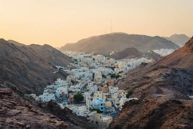 A town of white buildings nestled in a valley surrounded by rocky mountains at sunset.