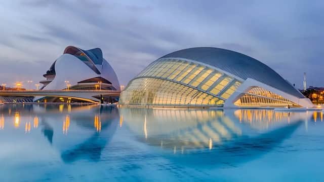 Due edifici moderni e illuminati con architettura curvilinea che si riflettono in un grande e calmo specchio d'acqua al tramonto.