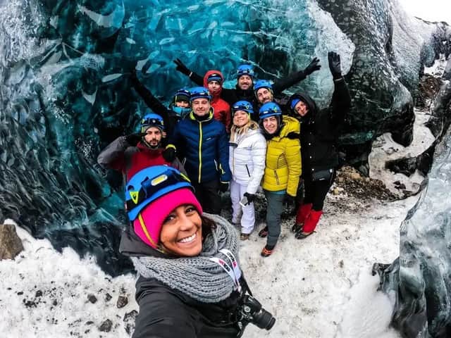 Un viaje en grupo de WeRoad con cascos y chaquetas de invierno sonríe para una selfie dentro de una cueva de hielo azul translúcida.