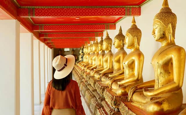 Una donna con un cappello di paglia cammina lungo un corridoio di tempio fiancheggiato da una lunga fila di statue dorate di Buddha.