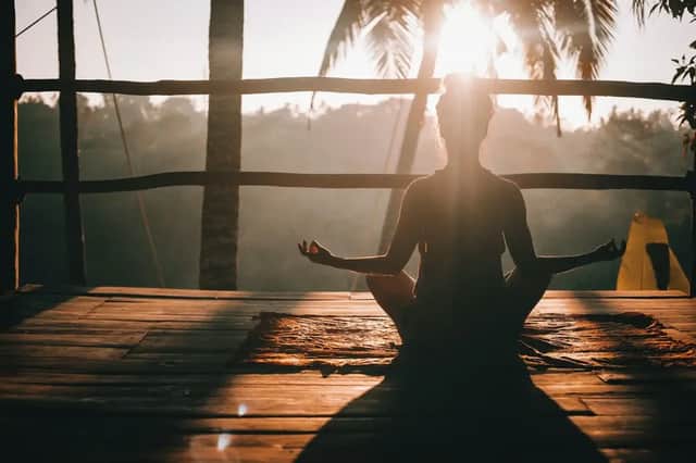 Una persona in silhouette siede in posizione di meditazione su un portico di legno mentre il sole sorge dietro le palme.