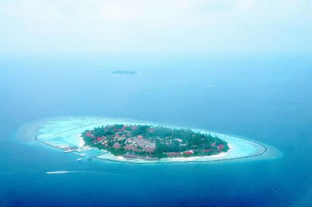 Vue aérienne d'une petite île tropicale luxuriante avec un complexe hôtelier, entourée d'eaux turquoises et de l'océan d'un bleu profond.