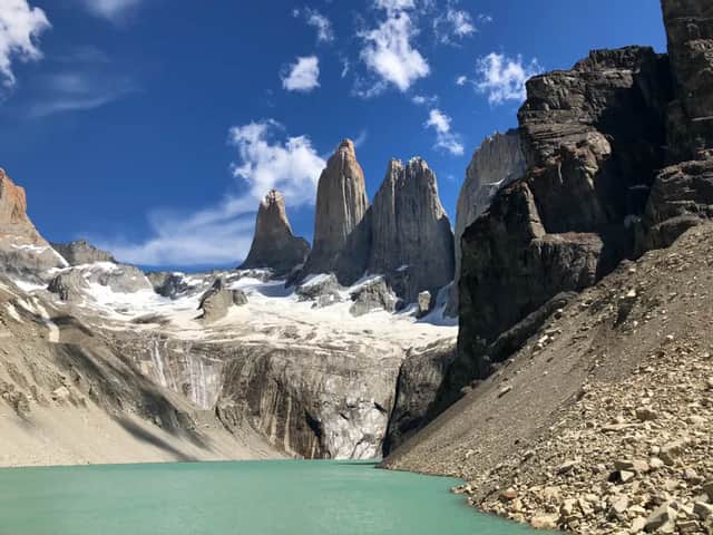 Trois sommets de granit déchiquetés et un glacier dominant un lac glaciaire turquoise sous un ciel bleu éclatant avec des nuages clairsemés.
