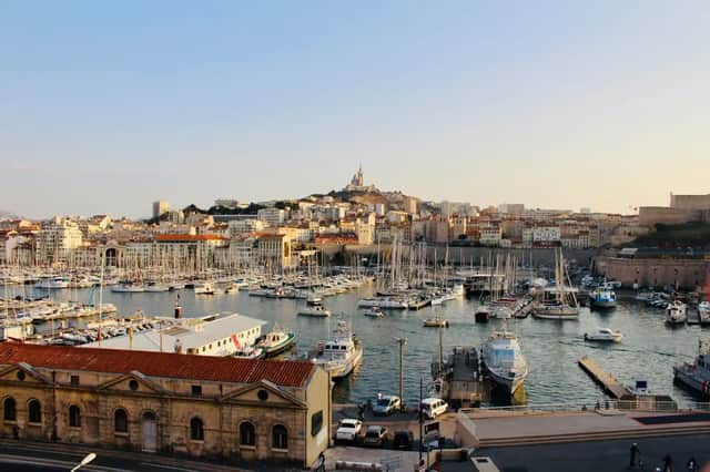 Un vaste port rempli de voiliers et de yachts, avec une ville historique et une basilique sur une colline lointaine.
