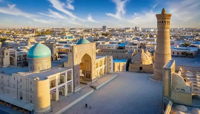 Vista aérea de una plaza histórica con una cúpula turquesa y un minarete alto al amanecer.