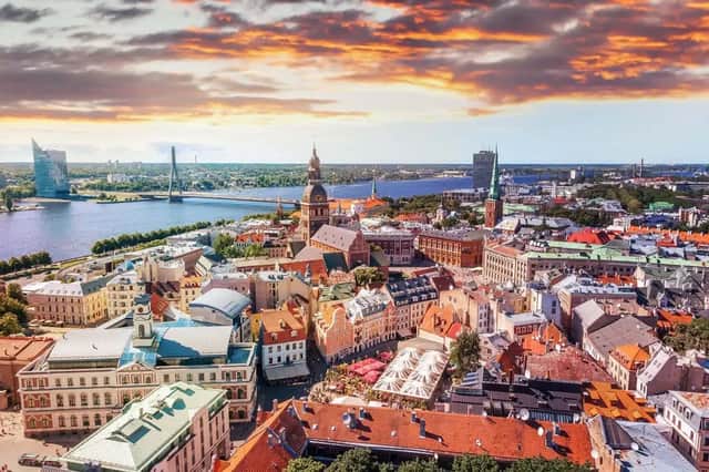 Luftaufnahme einer historischen Stadtlandschaft mit roten Dächern und Kirchtürmen entlang eines breiten Flusses unter einem farbenprächtigen Sonnenuntergangshimmel.