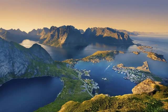 Panoramablick auf Küstendörfer auf grünen Inseln, umgeben von Fjorden und zerklüfteten Bergen unter goldenem Himmel.