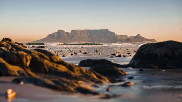 Une montagne au sommet plat se dresse face à l'océan, vue depuis une plage rocailleuse et mouillée sous un coucher de soleil doré.