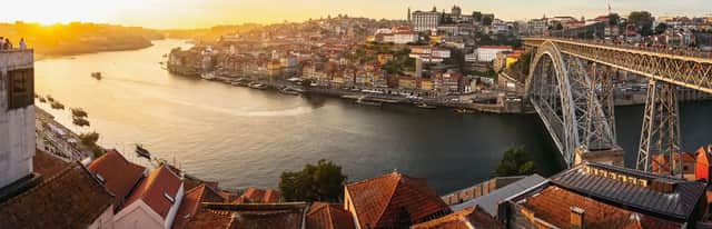 Una vista panoramica di una città sul fiume al tramonto, con un grande ponte ad arco e colorati edifici sulle colline.