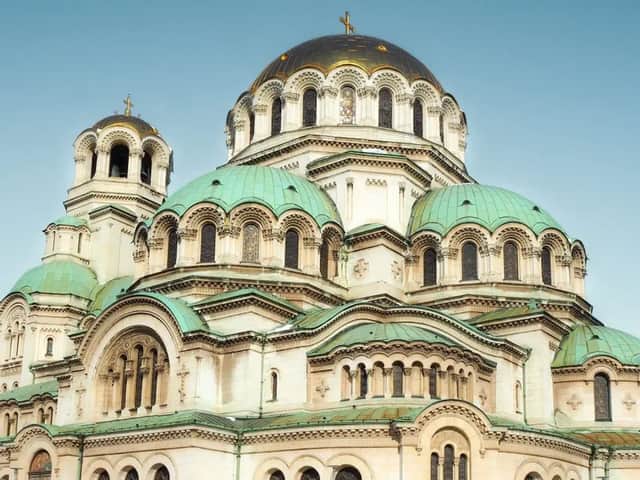 A large cathedral with a central golden dome and multiple green domes against a clear blue sky.