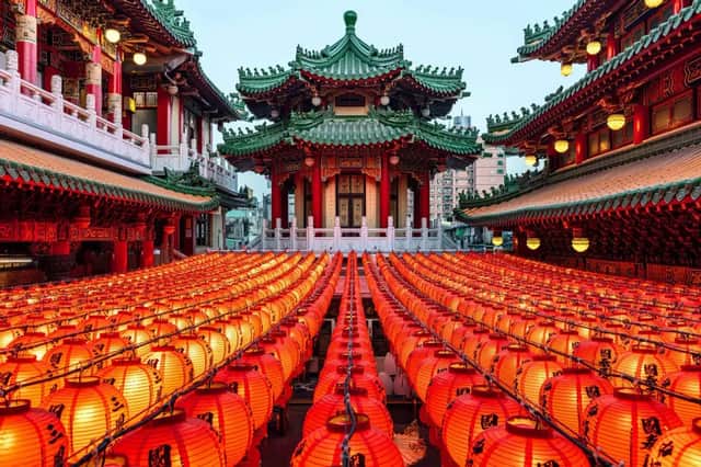 Des rangées de lanternes en papier rouges et lumineuses remplissent une cour devant un temple traditionnel d'Asie de l'Est avec un toit vert de style pagode.