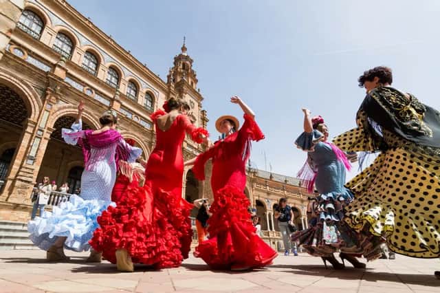 Un groupe de femmes en robes de flamenco traditionnelles et colorées dansant sur une place ensoleillée devant un bâtiment orné.