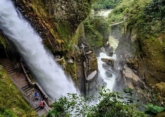 Ein mächtiger Wasserfall, der eine felsige Schlucht hinabstürzt, neben einer gewundenen Steintreppe, auf der Menschen gehen.