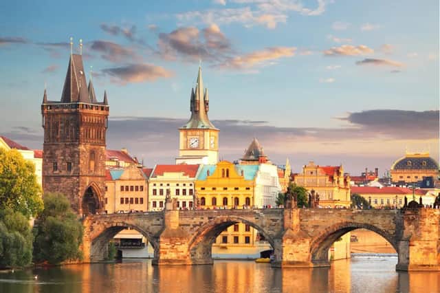 Un pont en arc en pierre historique avec une tour gothique enjambe une rivière devant la ligne d'horizon d'une ville européenne au coucher du soleil.