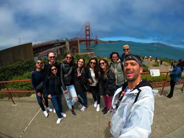 Un groupe WeRoad prend un selfie depuis un point de vue, avec un grand pont suspendu rouge et la mer en arrière-plan.
