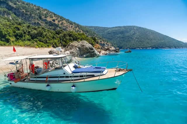 Un viaje en grupo de WeRoad relajándose en un barco anclado en aguas cristalinas de color turquesa, con una playa y colinas verdes de fondo.