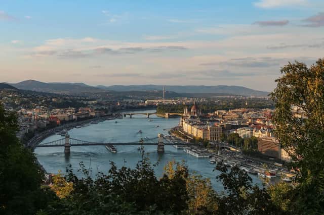 Una veduta aerea di una città attraversata da un grande fiume, solcato da diversi ponti, con colline sullo sfondo sotto un cielo blu.