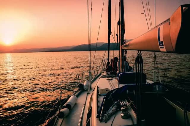 Eine WeRoad-Gruppenreise an Deck eines Segelboots, die einen orangefarbenen Sonnenuntergang über dem Wasser mit fernen Bergen genießt.