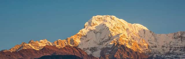 Una grande cima montuosa coperta di neve illuminata dalla luce dorata del sole contro un cielo azzurro e limpido.