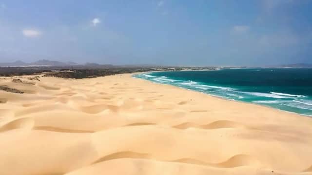 Vastas dunas de arena dorada descienden hasta el encuentro de las olas turquesas del océano a lo largo de una extensa costa.