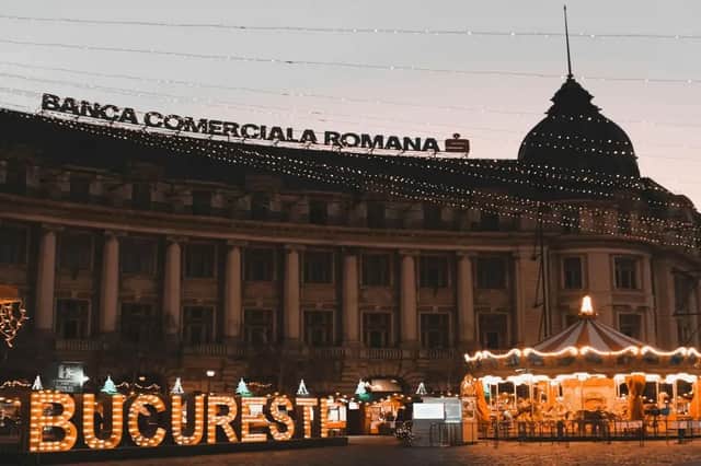 Una piazza cittadina al tramonto con un'insegna 'BUCURESTI' illuminata, una giostra e un edificio con lucine.